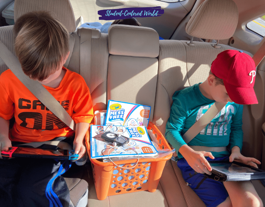 Two Generation Alpha kids sit in the back seat, each absorbed in their own device. One sports an orange shirt, the other a red cap and teal shirt. Between them lies an orange basket holding a children's activity book, capturing the essence of their tech-savvy world.