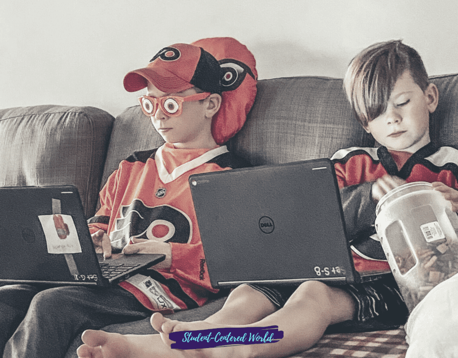 Two Generation Alpha kids sit on a couch using laptops, both in hockey jerseys and caps. One munches snacks from a jar while the other sports funny glasses. A pillow featuring their team's logo is nestled behind them.